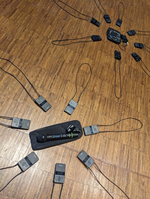 Als Verbindungsbeispiele auf dem Boden ausgebreitet liegen 7 Empfängerkästchen um ein Handmikrofon herum. Dahinter ebenfalls auf dem Boden zu sehen, liegen 8 Empfängerkästchen um ein Headset herum. Sie stellen zwei Wege dar, Ton zu senden. Dabei können zum Beispiel gleichzeitig verschiedenen Personen in einer Gruppe auf einem bestimmten Kanal nur den Ton ihres Senders hören, während die andere Empfängergruppe etwas anderes hört.